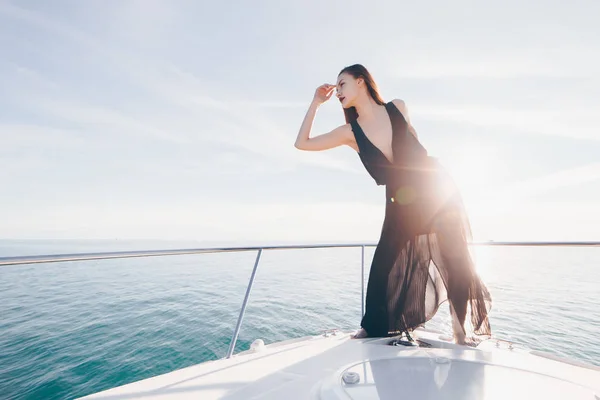 An attractive girl in black summer clothes posing on a ship in the sun, enjoys sea voyage — Stock Photo, Image