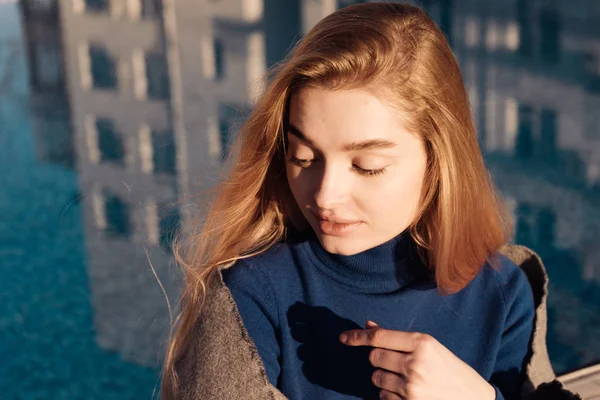 Prachtig mooie blonde meisje in een blauwe trui rust bij het zwembad in de zon, ontspannen — Stockfoto