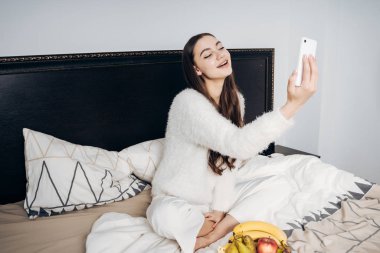 güzel uzun saçlı kız selfie onu Smartphone'da yapma yatakta oturmuş pijama