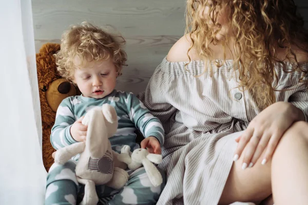 Curly little baby boy in blue pajamas sitting next to his mom and playing in toys — Stock Photo, Image