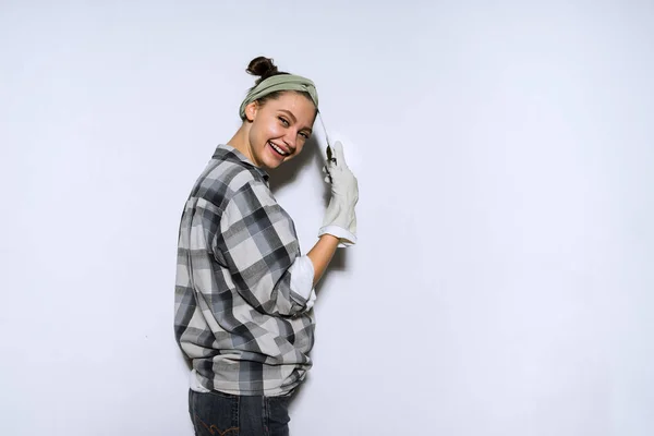 Young smiling girl in plaid shirt doing repairs in apartment, painting walls — Stock Photo, Image