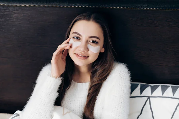 Attraktives junges Mädchen sitzt frühmorgens im Bett, unter den Augen weiße Flecken, gute Laune — Stockfoto