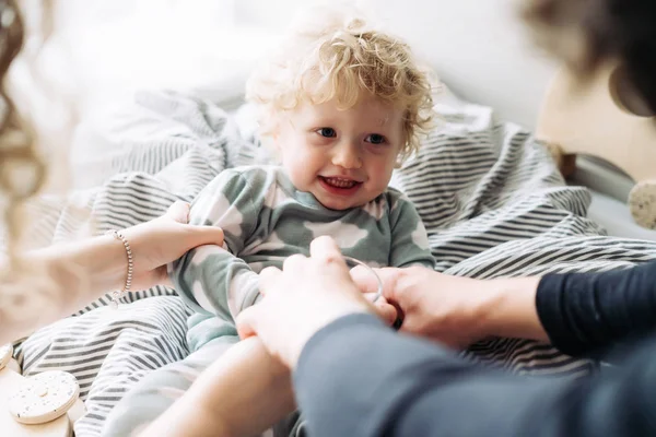 parents play with their little curly-haired son in pajamas, laugh and have fun