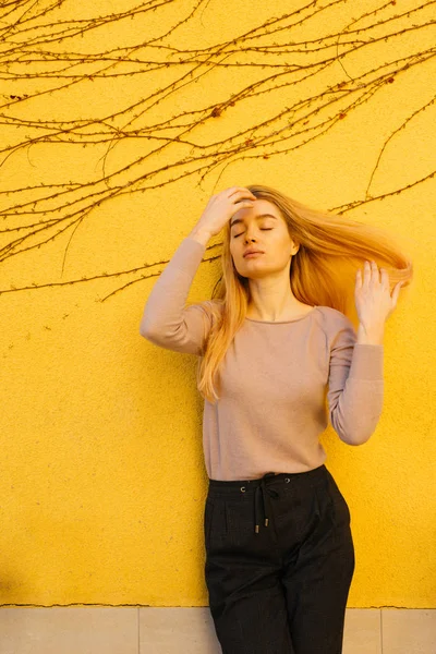 Fashionable young blonde girl posing on yellow background in stylish clothes — Stock Photo, Image