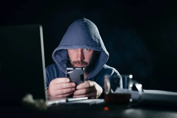 Mysterieuze bebaarde man hacker in de kap zit in de donkere, barst het wachtwoord op de telefoon — Stockfoto