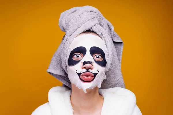 funny young girl with a towel on her head posing, on her face a moisturizing mask with a panda face