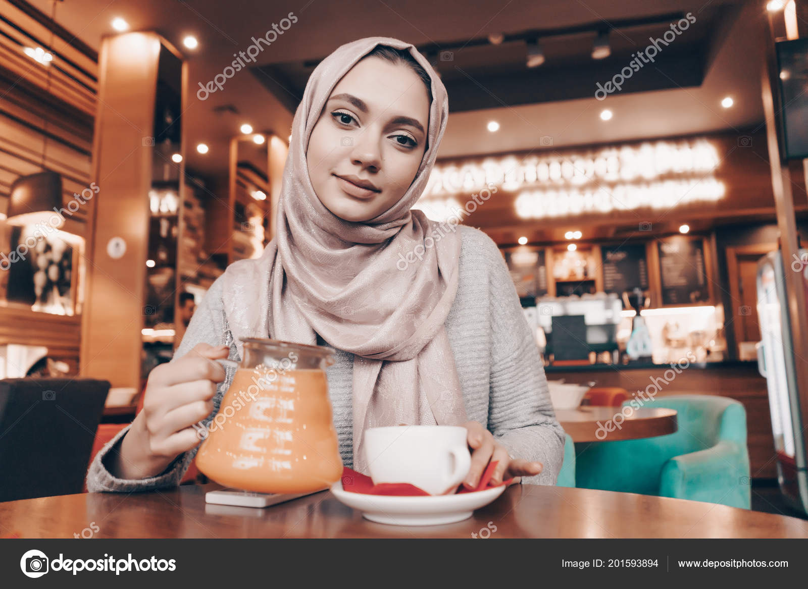 Nice Arab girl with a headscarf sitting in a cozy restaurant, drinking