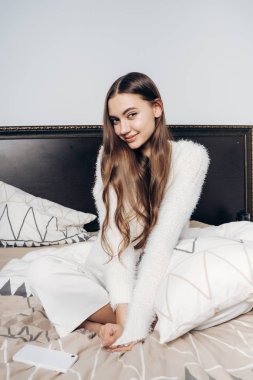 Pijama uzun saçlı, uzun saçlı bir kız yatakta oturur, iyi bir ruh hali sabah erkenden uyandım