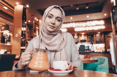 bir başörtüsü rahat bir restoranda oturan, çay içme ve yemek güzel Arap kızla