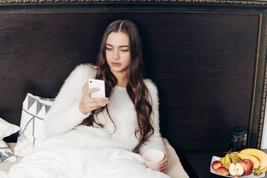 uzun saçlı güzel kız akşamları yatakta yatıyor, onu smartphone görünüyor