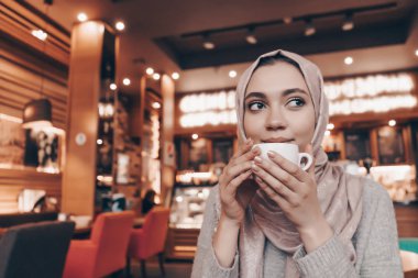 kafasındaki bir başörtüsü ile şirin bir Müslüman kız güzel kokulu sıcak kahve bir kafede içecekler.