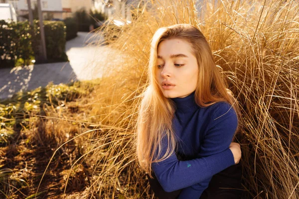 Mladá krásná blond model dívka v módní modrý svetr pózuje na slunci v ulicích města — Stock fotografie