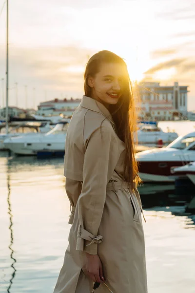 Bela menina de cabelos longos goza da vista para o mar no porto ao pôr do sol, sorrindo — Fotografia de Stock