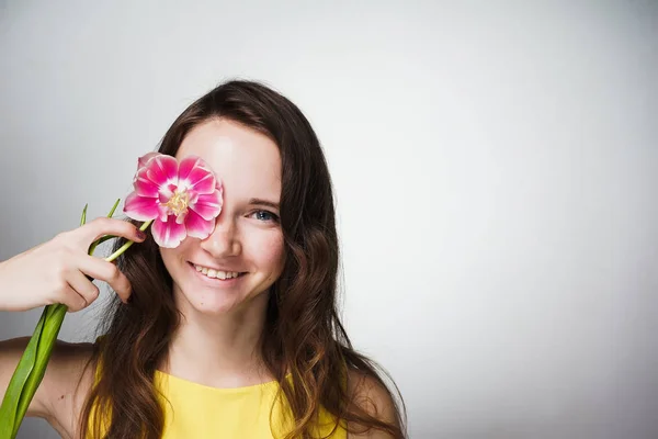 Carina bella ragazza sorridente che tiene un fiore rosa fragrante vicino al viso — Foto Stock