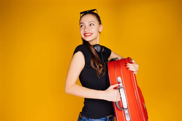 Felice ragazza sorridente in una t-shirt nera va in vacanza con una grande valigia rossa — Foto Stock