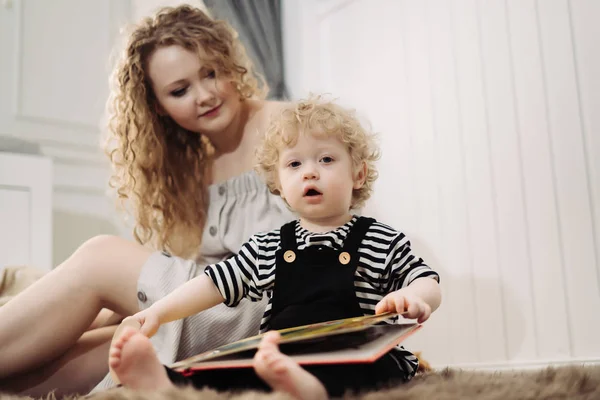 Una familia unida, un pequeño niño de pelo rizado se sienta al lado de su madre, lee un libro — Foto de Stock