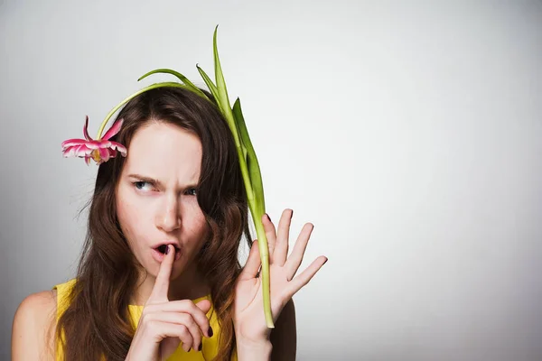 Una joven descontenta con un vestido amarillo puso su dedo en sus labios, sostiene una flor fragante — Foto de Stock