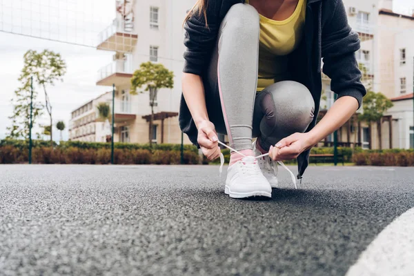 Atletisk flicka zazyayvaet skosnören på sina sneakers på en idrottsplats utomhus, kommer att köra — Stockfoto