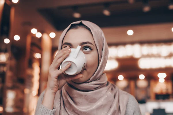 Ein nettes muslimisches Mädchen mit Kopftuch sitzt in einem gemütlichen Restaurant und trinkt duftenden Kaffee — Stockfoto