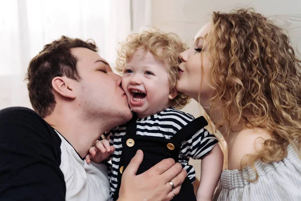 Familia alegre amistosa, padres jóvenes, padre y madre abrazan a su pequeño hijo de pelo rizado — Foto de Stock