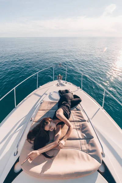 Una donna attraente in abiti estivi neri si trova sul suo yacht al sole, si rilassa e si rilassa — Foto Stock