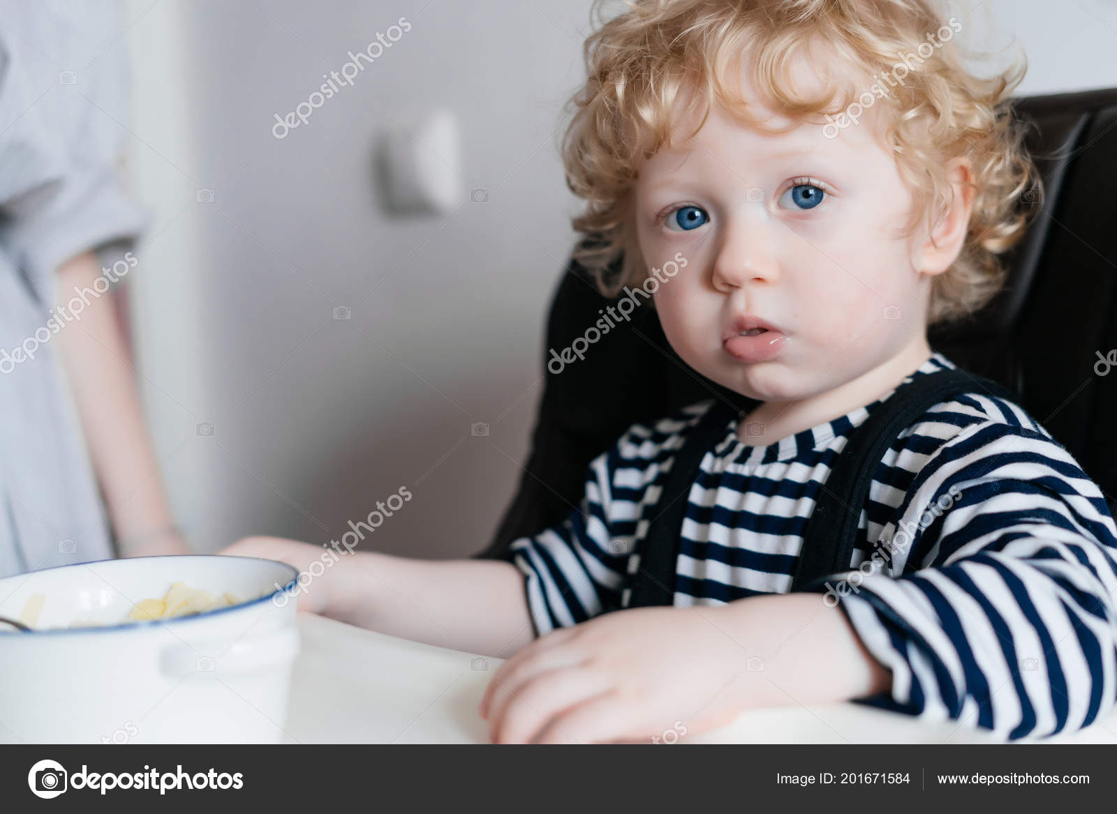 Curly blonde blue-eyed boy sits in the kitchen, eats useful cereal Stock  Photo by ©mne_len 201671584