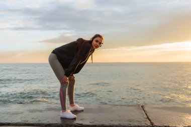 gün batımında, deniz kenarında yürüyüş sonra dinlenme etkin kız runner kulaklıklar müzik dinlemek