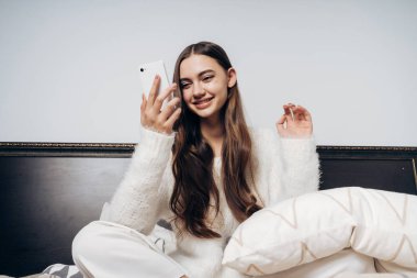 Sabahın erken saatlerinde, görünüyor onun smartphone, iyi bir ruh hali içine uzun saçlı tatlı gülümseyen kız uyandı