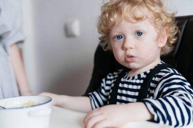 Kıvırcık sarışın mavi gözlü çocuk mutfakta oturuyor, yararlı Mısır gevreği yiyor