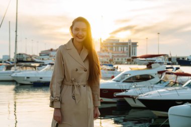 mutlu gülümseyen kız moda bej bir palto günbatımında liman içinde poz uzun saçlı