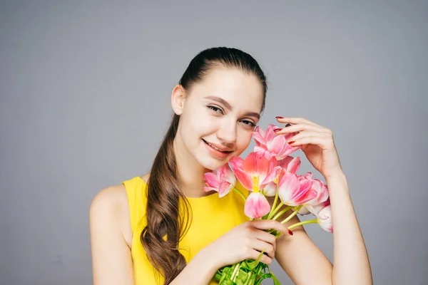 Aantrekkelijke lachende vrouw in gele jurk houdt geurige roze bloemen en poses — Stockfoto