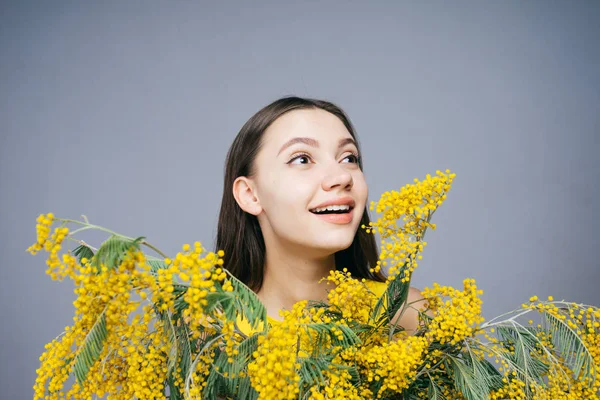 Beautiful young girl holding an aromatic yellow mimosa, smiling and enjoying the spring — Stock Photo, Image