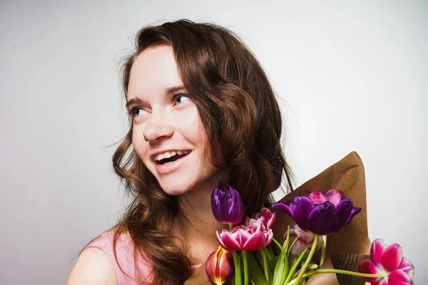 Hermosa mujer de pelo largo sonriendo y disfrutando de la primavera, sosteniendo un ramo de flores fragantes — Foto de Stock