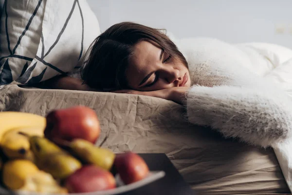 Uma jovem de pijama branco jaz na cama sob um cobertor branco, dormindo, de manhã cedo — Fotografia de Stock