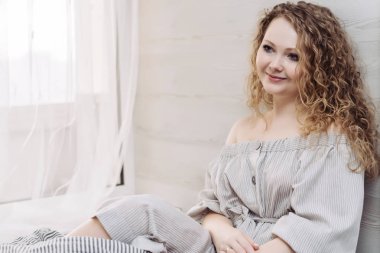 Cam kenarında oturan ve gülümseyen bir elbise kıvırcık çekici genç kadın