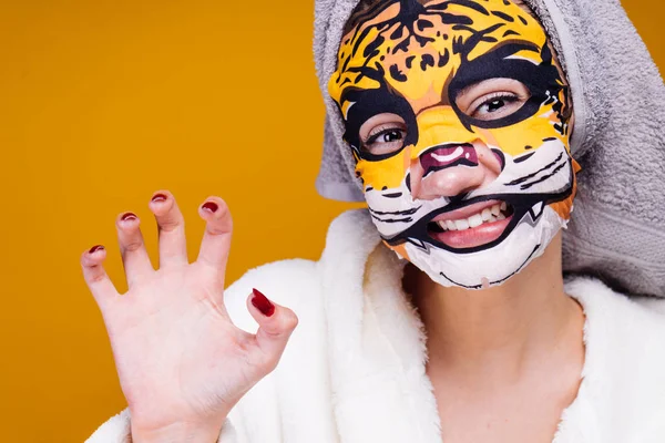 Una joven divertida quiere ser hermosa, en su cara una máscara hidratante con una cara de leopardo, sonriendo —  Fotos de Stock