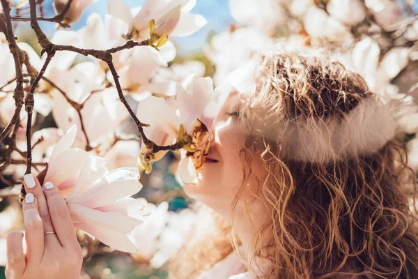 Hermosa mujer rizada olfateando una magnolia floreciente fragante en un parque en los rayos del sol — Foto de Stock