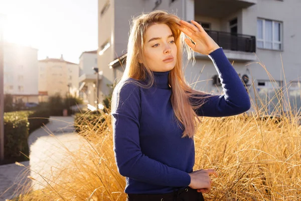 戸外で太陽の下でポーズをとっておしゃれな青いセーターの若い美しいブロンド モデル女の子 — ストック写真