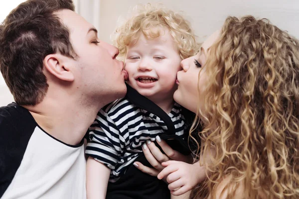 friendly happy family, young parents, mom and dad kiss their little curly son