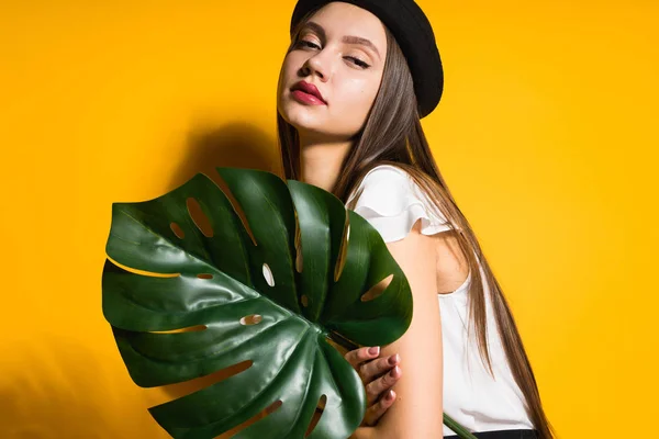 Confiado hermosa chica de pelo largo en negro elegante sombrero sostiene una hoja verde y posa — Foto de Stock