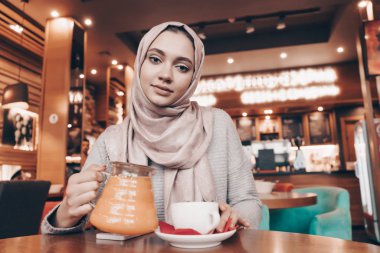 bir başörtüsü başında bir güzel Arap kızla rahat bir kafede dines, çay içiyor ve kameraya dumanlar