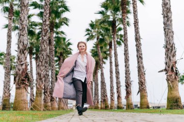 uzun bir ceket neşeli aktif genç kadın parkta yürüyor ve sıcak bahar hava sahiptir