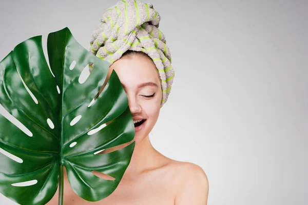 Hermosa joven con una toalla en la cabeza cubierta su cara con una hoja verde — Foto de Stock