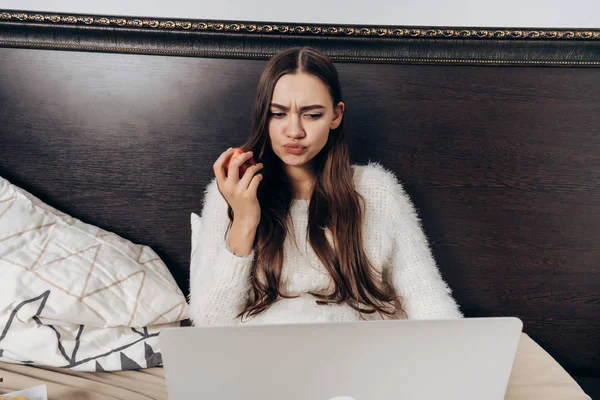 Ontevreden langhaar meisje in pyjama 's avonds laat in bed zitten, kijken naar een interessante film en eten van een appel — Stockfoto