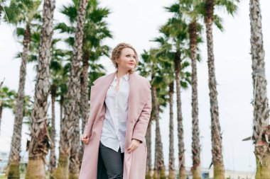 şık genç kadın uzun boylu avuç içi yanında yeşil bir park boyunca yürüyüş pembe bir ceket