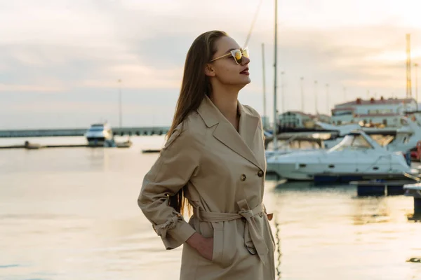 Atractiva chica de pelo largo en abrigo elegante y gafas de sol posando en el puerto — Foto de Stock