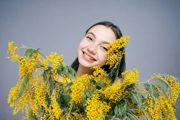 Attractive smiling young girl holding a bouquet of fragrant yellow mimosa, posing — Stock Photo, Image