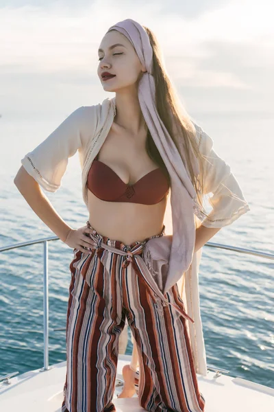 Atractiva chica con estilo en ropa de verano posando en su yate, disfrutando de vacaciones y el aire del mar —  Fotos de Stock