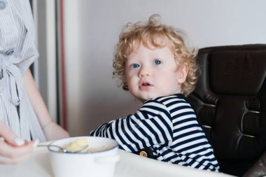 Mutfakta, lezzetli çorba besleme anne oturan küçük Kıvırcık sarışın mavi gözlü bebek çocuk