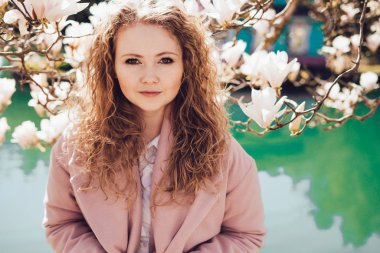 güzel kıvırcık genç kadın parkta blooming manolya ve gölet yanında poz